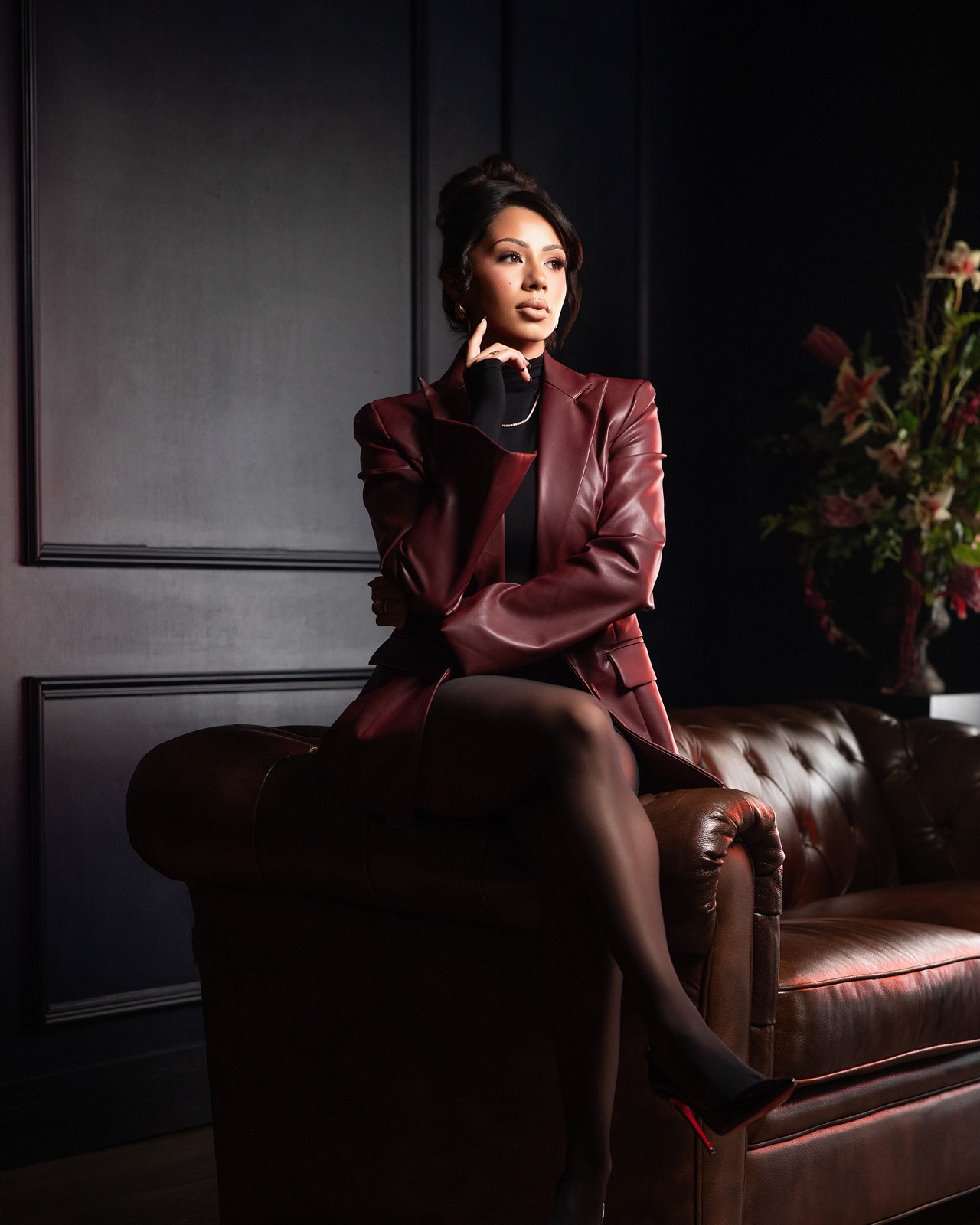 Founder seated on the arm of a burgundy leather sofa, looking away
